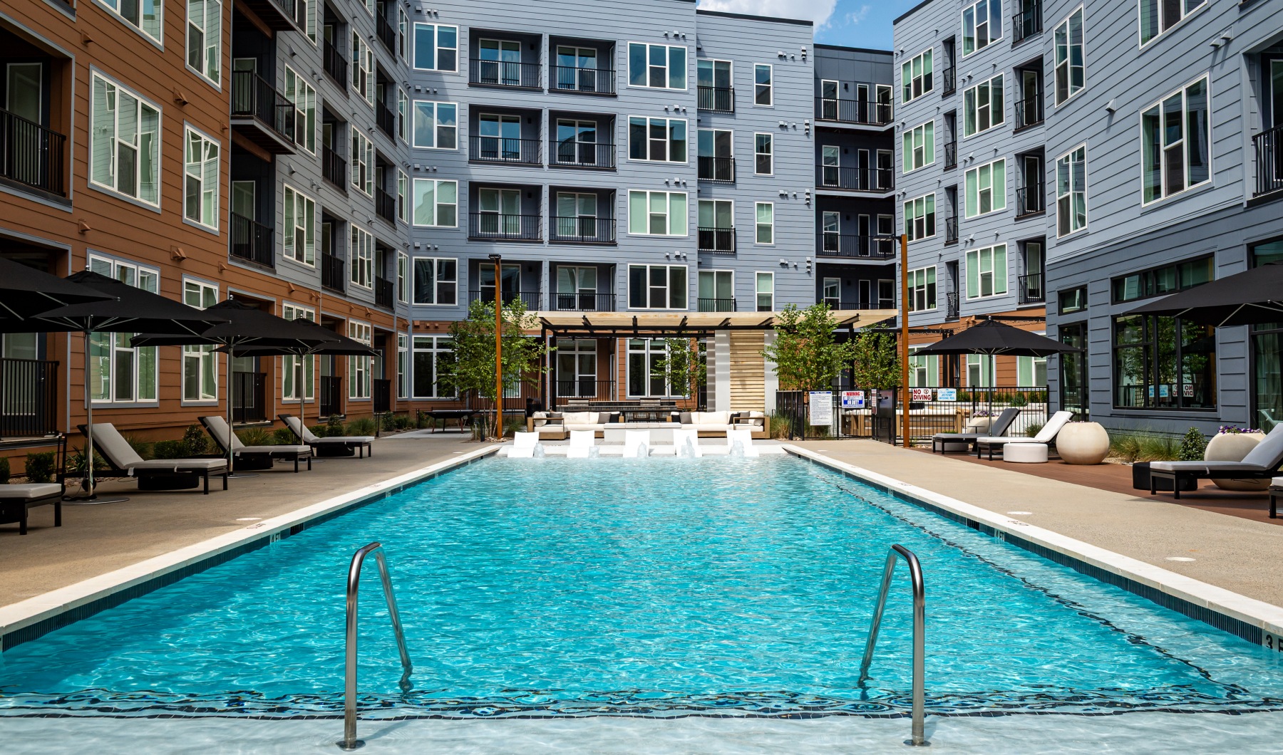 a pool in front of an apartment building with ample sun deck seating 