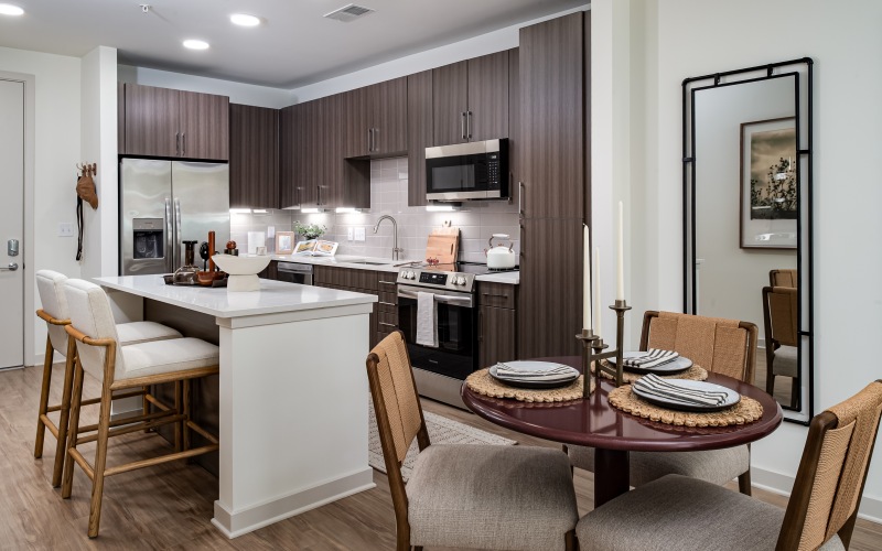 a dining table and chairs next to a kitchen space with an island with two bar  chairs 